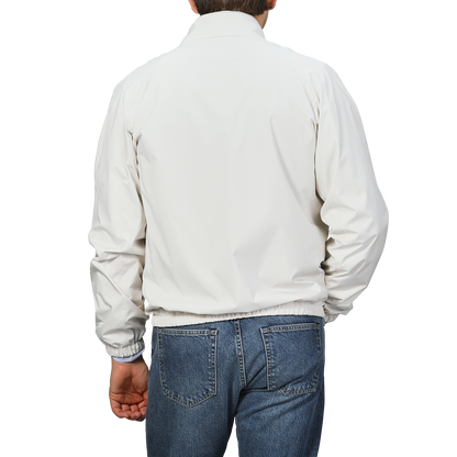 A person wearing a Fedeli Beige Nougat Nylon Reversible Blouson Jacket and blue jeans stands against a gray background, facing away from the camera.