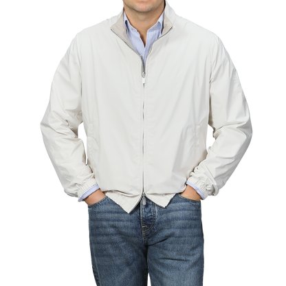 Man in a beige nougat nylon reversible Fedeli blouson jacket over a blue striped shirt with jeans, against a gray background.