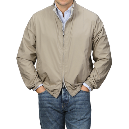 A person wearing a Fedeli Beige Nougat Nylon Reversible Blouson Jacket with a two-way zip closure, paired with blue jeans, stands with hands in pockets against a neutral background.