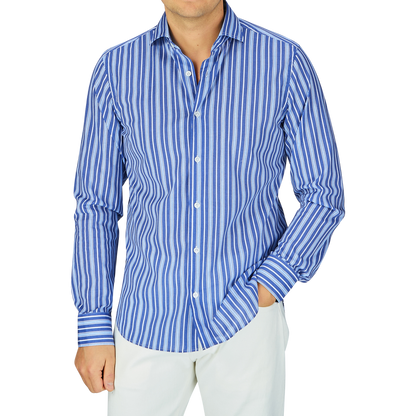 A man wearing a Fedeli dark blue striped cotton beach shirt with the sleeves rolled up, paired with white pants.