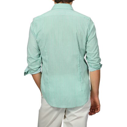A person wearing a Fedeli slim fit Green White Striped Cotton Beach Shirt with rolled-up sleeves and white pants faces away from the camera.
