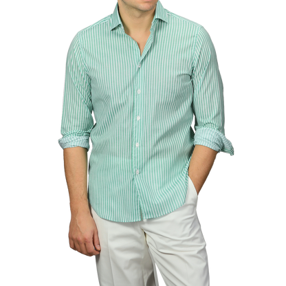 A person sporting a Fedeli Green White Striped Cotton Beach Shirt with rolled-up sleeves and slim-fit white pants stands with one hand in their pocket.