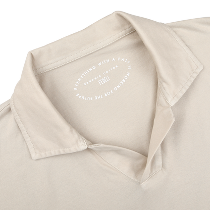 Close-up of the Light Beige Organic Cotton Capri Collar Polo Shirt by Fedeli shows an open capri collar and a visible inner label reading, "Everything with a past is working for future." Crafted from organic Giza cotton, it blends luxury casual-wear with sustainability.