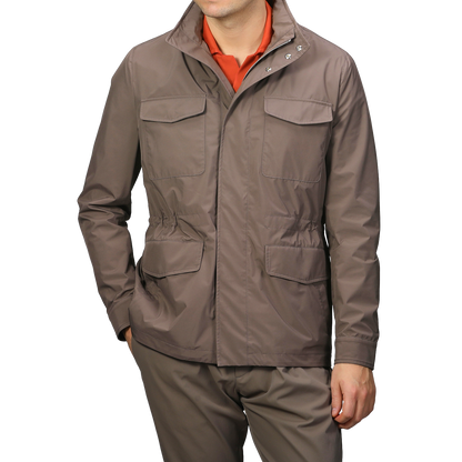 A person is wearing a Light Brown Nylon Rainproof Field Jacket by Fedeli, featuring multiple pockets and a slim fit, paired with matching pants. Beneath the wind and water-resistant jacket is an orange shirt, adding a pop of color to their outfit.