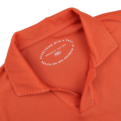 A close-up of the Fedeli Orange Organic Cotton Capri Collar Polo Shirt showcases its luxury casual-wear essence, with a printed circular label inside the collar.