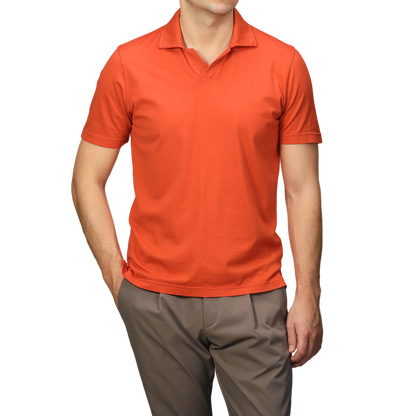 Elegantly attired in a Fedeli Orange Organic Cotton Capri Collar Polo Shirt and brown pants, a person stands out against a neutral backdrop.