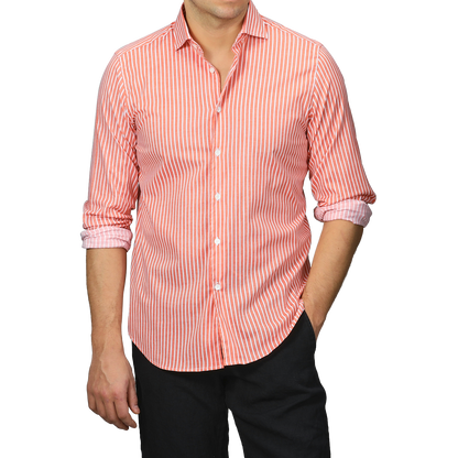 Dressed in a slim fit Orange White Striped Cotton Beach Shirt by Fedeli, a person with rolled-up sleeves stands stylishly against a plain background, paired elegantly with black pants.