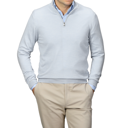 A person wearing a Fedeli Sky Blue Cashmere Silk 1/4 Zip Sweater stands with hands in pockets against a plain background, complemented by a light gray shirt and beige pants.