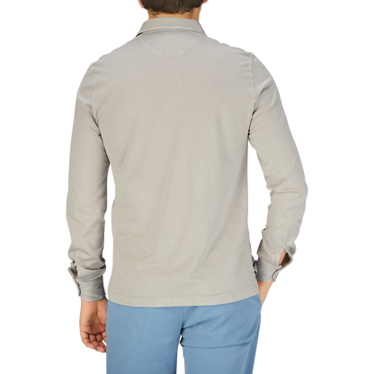 The back view of a man wearing a Fedeli Taupe Beige Organic Cotton LS Polo Shirt and blue pants.