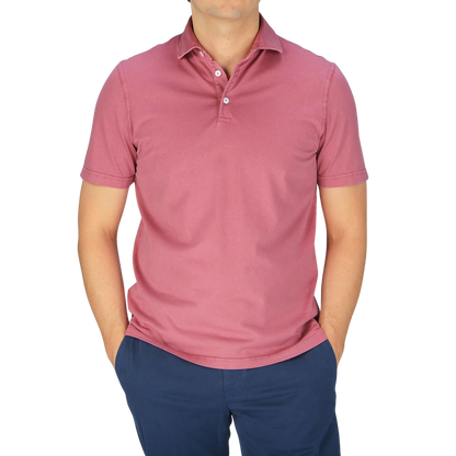 A man wearing a Fedeli washed raspberry organic cotton polo shirt and blue pants.