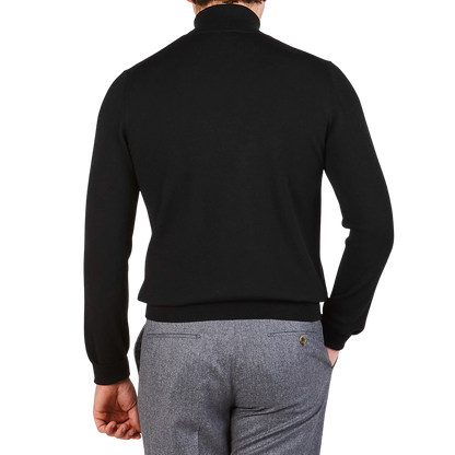 A man is seen from behind wearing a Gran Sasso Black Extra Fine Merino Wool Rollneck and gray pants against a plain white background.