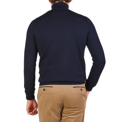 A person wearing a Gran Sasso Navy Blue Extra Fine Merino Wool Rollneck and beige pants stands with their back to the camera against a plain background.