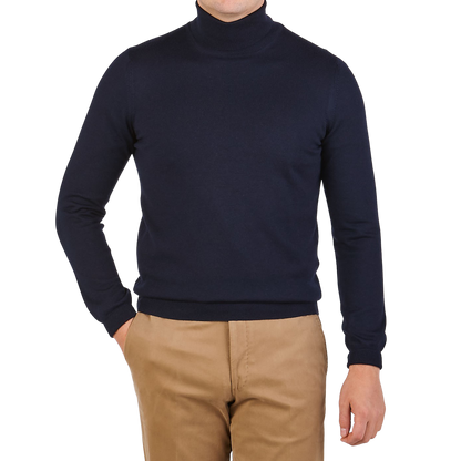 A person wears the Gran Sasso Navy Blue Extra Fine Merino Wool Rollneck with tan pants, standing against a plain background with one hand in their pocket.
