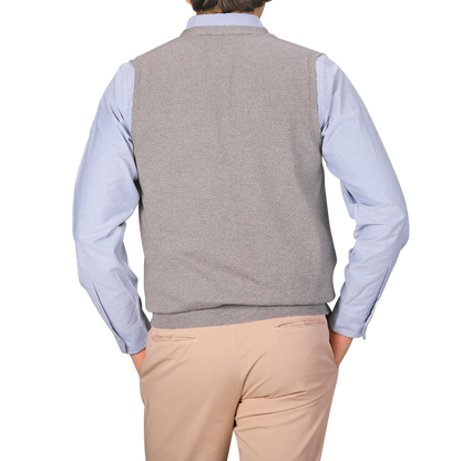 A person is shown from the back, hands in pockets, wearing a light blue dress shirt and Gran Sasso's Beige Extra Fine Merino Wool Vest, paired with beige pants against a plain background.