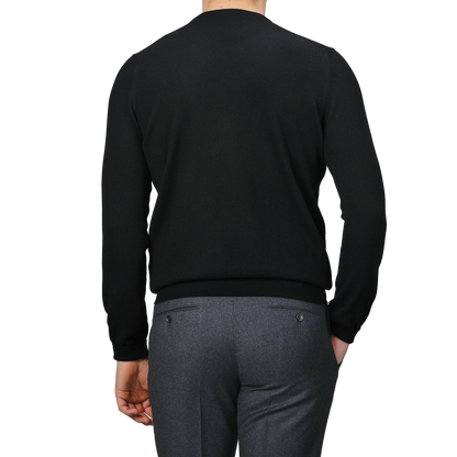 A person is wearing a black cashmere crewneck sweater by Gran Sasso and gray pants, viewed from behind.