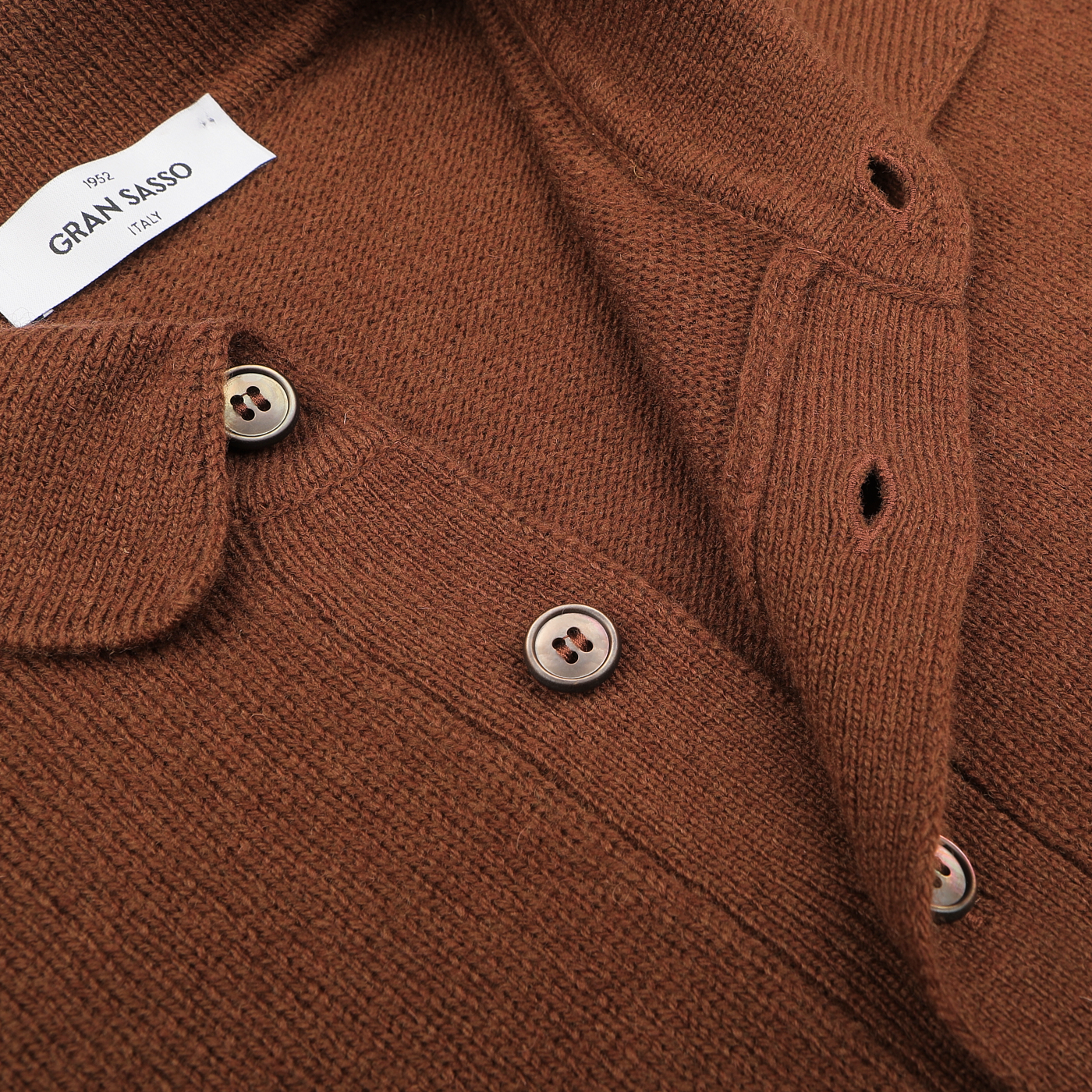 Close-up of a burnt orange long-sleeve polo shirt, crafted from pure virgin wool, with visible buttons and buttonholes. It features a label that reads "Gran Sasso Italy.
