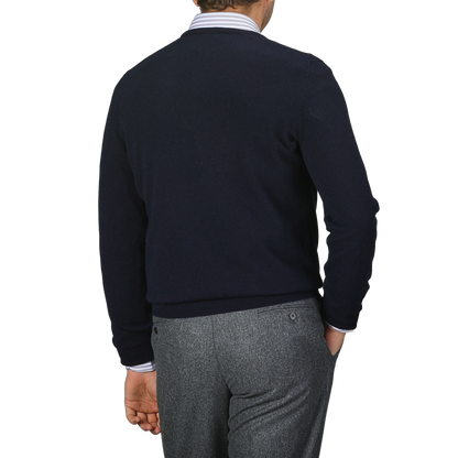 A person in a Navy Blue Cashmere Crew Neck Sweater by Gran Sasso and gray trousers is facing away, highlighting the back of this stylish outfit against a plain background.