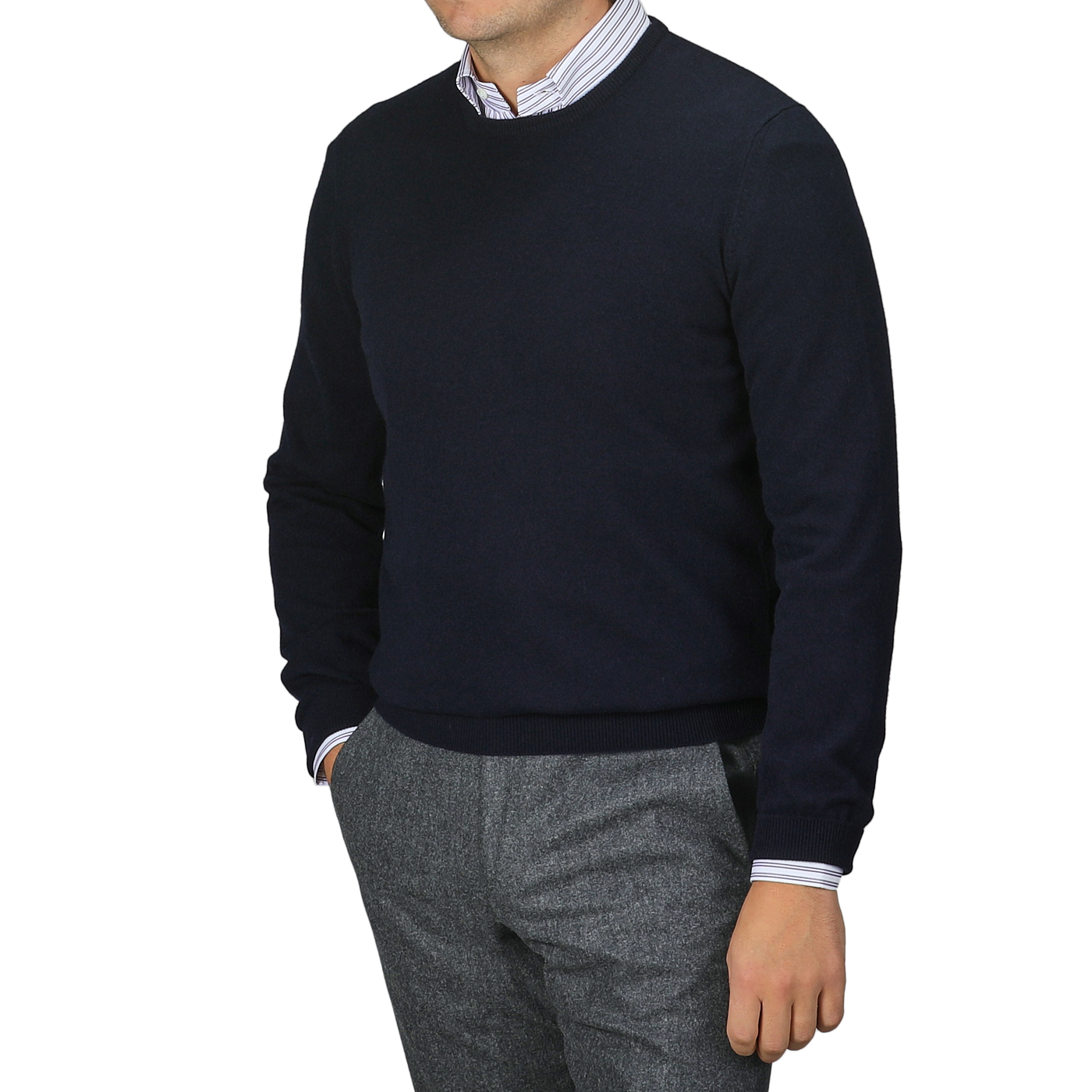 Clad in a Gran Sasso Navy Blue Cashmere Crew Neck Sweater and striped shirt, paired with gray pants, a person stands against a plain backdrop. This sustainable knitwear ensemble blends style and responsibility seamlessly, though their face remains unseen.