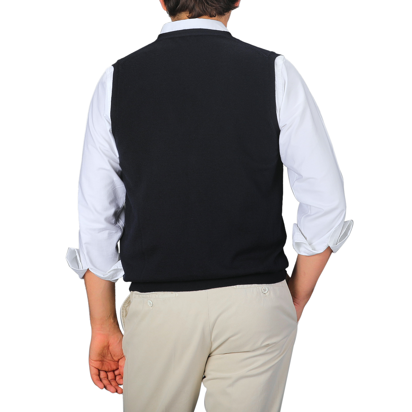 A person stands facing away, layering a white long-sleeve shirt with rolled-up sleeves and the Gran Sasso Navy Blue Extra Fine Merino Wool Vest over beige pants against a gray background.
