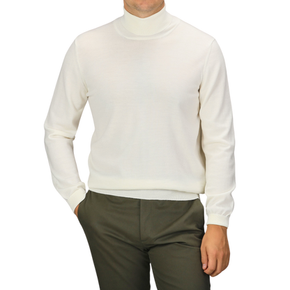 A person wearing an Off White Extra Fine Merino Rollneck by Gran Sasso and olive pants stands with one hand in their pocket against a plain background.