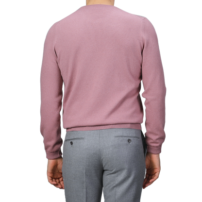 A person wearing a Gran Sasso Pale Pink Cashmere Crewneck Sweater and gray pants, photographed from the back against a gray background, embodies the elegance of sustainable knitwear.