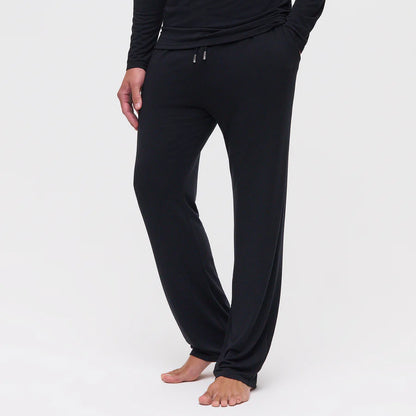 A person stands barefoot against a white background, displaying the relaxed fit and soft drape of Homebody’s Black Modal Modern Pyjama Trousers with a drawstring waist—ideal for those seeking comfortable men’s sleepwear. , available at Richard Gelding Mayfair