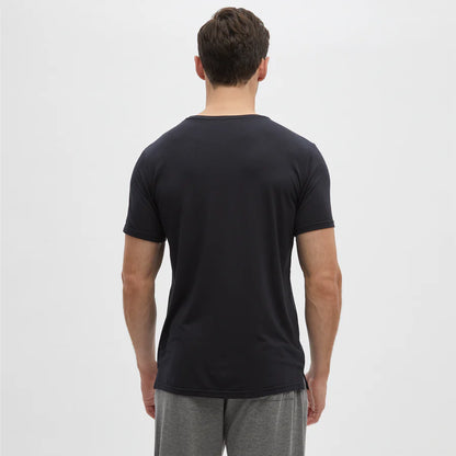 A man stands with his back to the camera against a plain white background, wearing a fitted Homebody Black Modal Classic Short Sleeve T-Shirt and gray shorts. His arms are relaxed at his sides, and his short hair is neatly styled. , available at Richard Gelding Mayfair