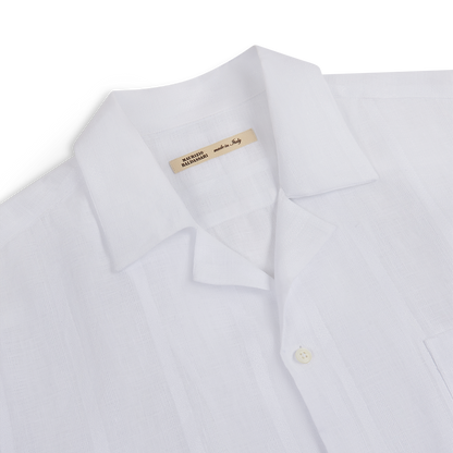 A close-up of the Maurizio Baldassari White Linen Short Sleeve Bowling Shirt, featuring a chest pocket, visible white button, and a “Made in Italy” tag inside the collar; set against a plain white background. , available at Richard Gelding Mayfair