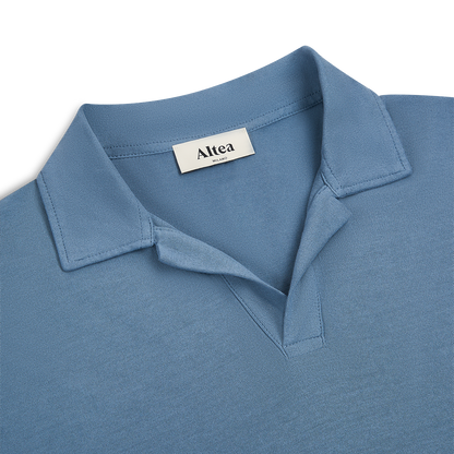 A close-up of the Altea Blue Ice Cotton Polo, crafted from soft light blue cotton, showcases its open collar for a casual, relaxed look against a white background. , available at Richard Gelding Mayfair