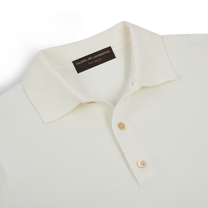 A close-up of the Filippo de Laurentiis Cream Sea Island Cotton Polo Shirt shows its ribbed collar, two beige buttons, and a black brand label inside the neck, all crafted in luxurious cotton and laid flat on a white surface. , available at Richard Gelding Mayfair