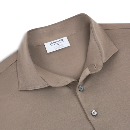The Gran Sasso Taupe Filo Scozia Polo for Richard Gelding features a classic collar, two-button placket, and a garment tag. , available at Richard Gelding Mayfair