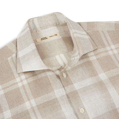 The Maurizio Baldassari Light Brown Linen Check Short Sleeve Shirt is shown laid flat. It features a spread collar, a subtle textured pattern, two front placket buttons, and a tag inside the collar reading “made in Italy.”. , available at Richard Gelding Mayfair