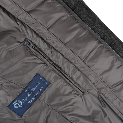 Close-up of the Charcoal Checked Wool Cashmere Loro Piana Jacket by Herno, highlighting the blue fabric label with white text and a zippered pocket detail within its lining. Crafted from a fine wool-cashmere blend, it provides extra comfort for those who value both style and functionality.
