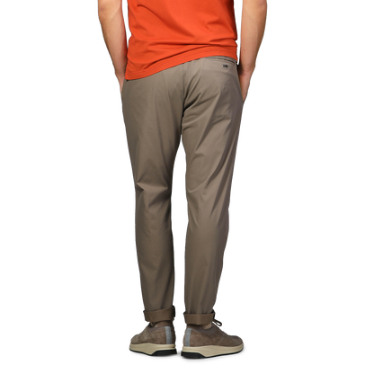 A person in an orange shirt stands with hands in pockets, facing away, wearing Herno's Dark Beige Nylon Stretch Drawstring Trousers.
