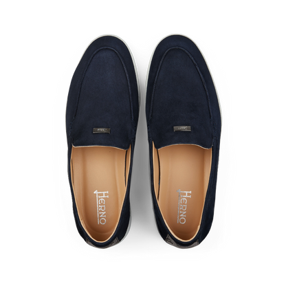 A pair of Herno dark blue suede slip-on loafers with a tan interior, displayed on a black background.