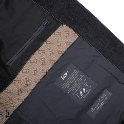 A close-up of the interior of the Herno Navy Blue Cashmere Silk Bomber Jacket reveals a lining adorned with patterns, labels, and pockets. The labels include care instructions and details about its luxurious cashmere and silk fabrics, as well as its water-repellent feature.