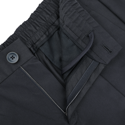 Close-up of slim fit navy blue nylon stretch trousers from Herno, featuring an elastic waistband with drawstring, button closure, and a visible zippered pocket.