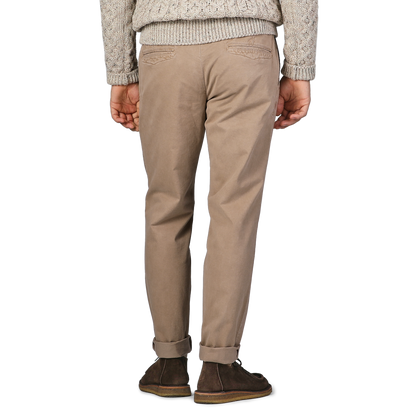 A person in Hiltl Beige Washed Cotton Gabardine Slim Chinos, a gray knit sweater, and brown shoes stands with their back to the camera.