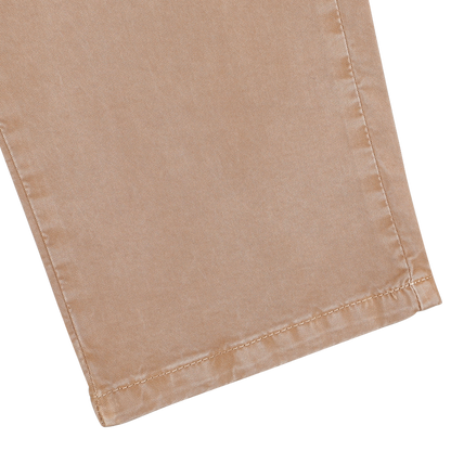 A close-up of the bottom hem of Hiltl's Beige Washed Cotton Gabardine Slim Chinos set against a gray backdrop, highlighting the refined texture characteristic of these light brown pants.