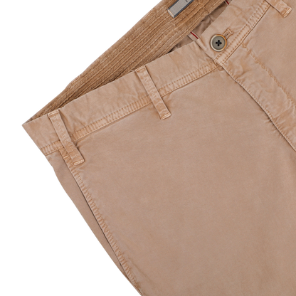 A neatly folded pair of Beige Washed Cotton Gabardine Slim Chinos by Hiltl, featuring a single button and belt loops, rests on a white surface.