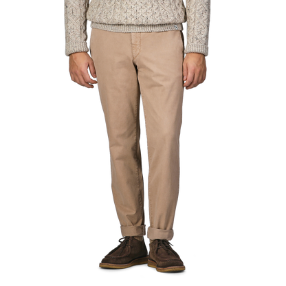 A person wearing a beige cable-knit sweater, Beige Washed Cotton Gabardine Slim Chinos by Hiltl, and dark brown shoes stands against a plain background.