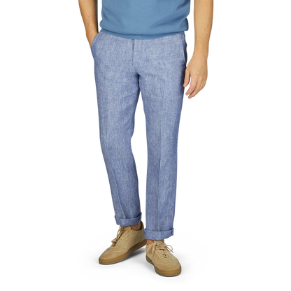 A man wearing light blue washed linen regular fit chinos from Hiltl and beige sneakers stands against a gray backdrop, with only the lower half of his body visible from the waist down.