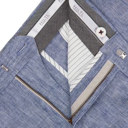 Close-up of an open blue denim jacket showing the inner Hiltl Light Blue Washed Linen Regular Fit Chinos lining, a label, and a partially zipped white inner layer.