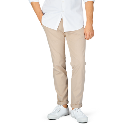 A person standing in a white shirt, Hiltl sand beige cotton nylon slim chinos, and white shoes against a gray background.