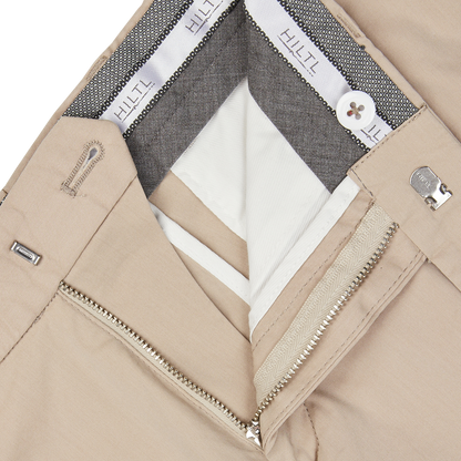Close-up of a Hiltl sand beige jacket with silver zipper detail, a gray inner lining, and a white shirt underneath, made from a cotton-nylon blend.