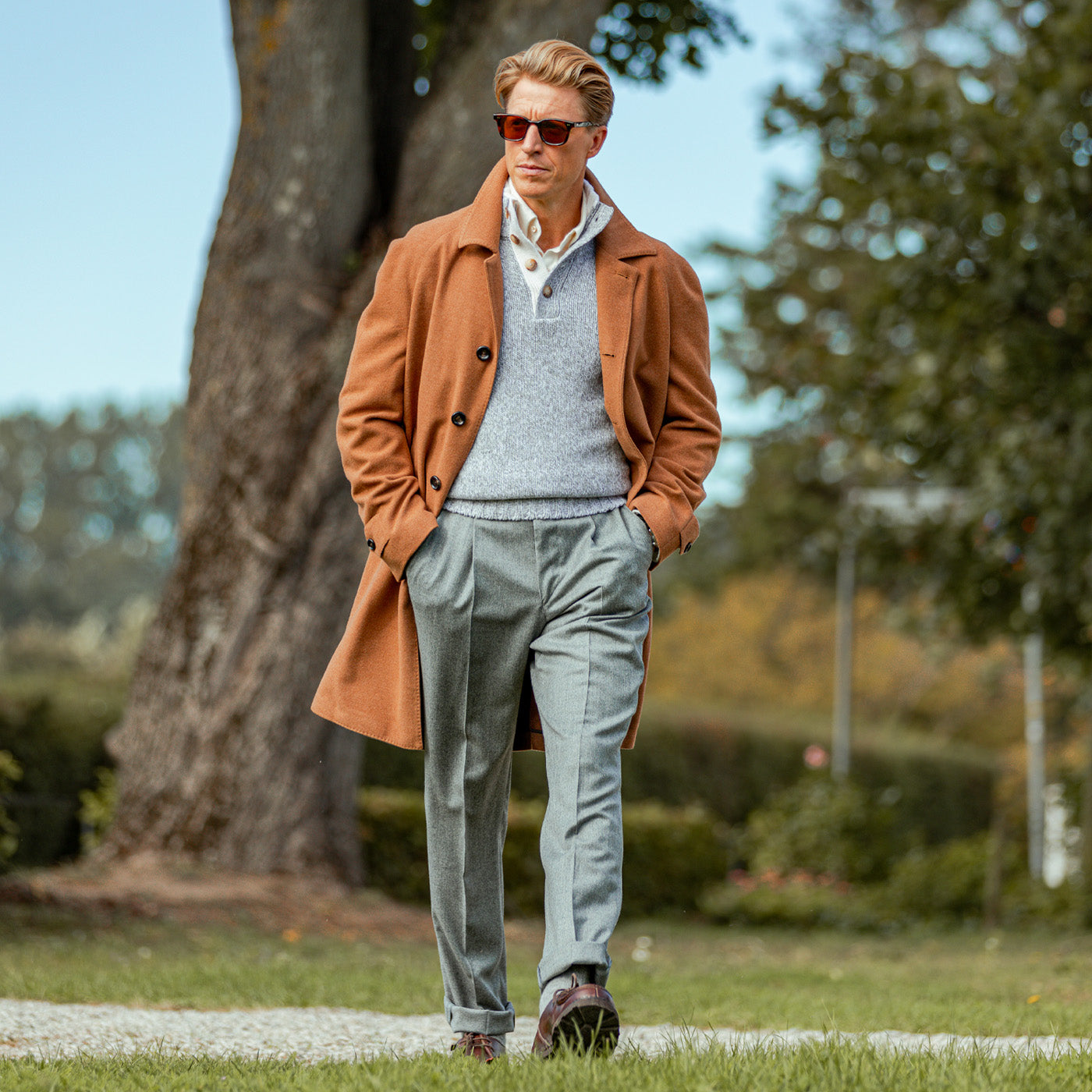 A man in a water-resistant Luigi Bianchi Camel Drago Skyfall Wool Raglan Coat walking through a park.