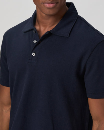 A man models a Paige Navy Pique Cotton Demille Short Sleeve Polo with three buttons undone, its textured cotton and tailored fit shown against a plain light background. The photo is cropped just below his nose. , available at Richard Gelding Mayfair