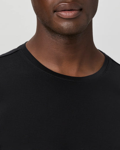 A close-up features the Paige Black Cotton Sorden Crew Neck T-Shirt worn by a person with smooth brown skin. The image captures their lower face, neck, and upper chest against a plain light background, highlighting the shirt’s simple style. , available at Richard Gelding Mayfair