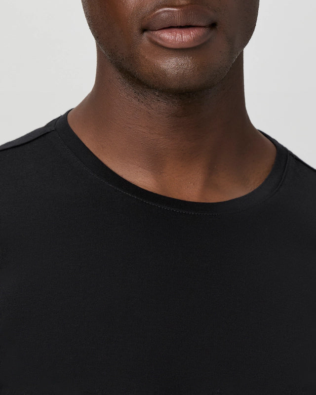 A close-up features the Paige Black Cotton Sorden Crew Neck T-Shirt worn by a person with smooth brown skin. The image captures their lower face, neck, and upper chest against a plain light background, highlighting the shirt’s simple style. , available at Richard Gelding Mayfair
