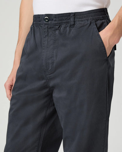 A close-up of someone wearing Paige Navy Cotton Stretch 'Eberton' Trousers with side pockets, high waist, and button closure, paired with a tucked-in white shirt and their right hand in the pocket. , available at Richard Gelding Mayfair